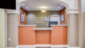 Ein Empfangsschalter mit einem Schild für MainStay Suites by Choice Hotels, dem Logo eines Sleep Inn und einem darüber montierten Fernseher.