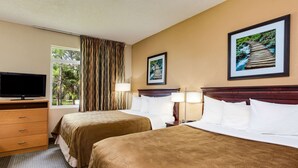 Ein Hotelzimmer mit zwei Betten, einem Fernseher, einem Schreibtisch und einem Fenster mit Vorhängen.