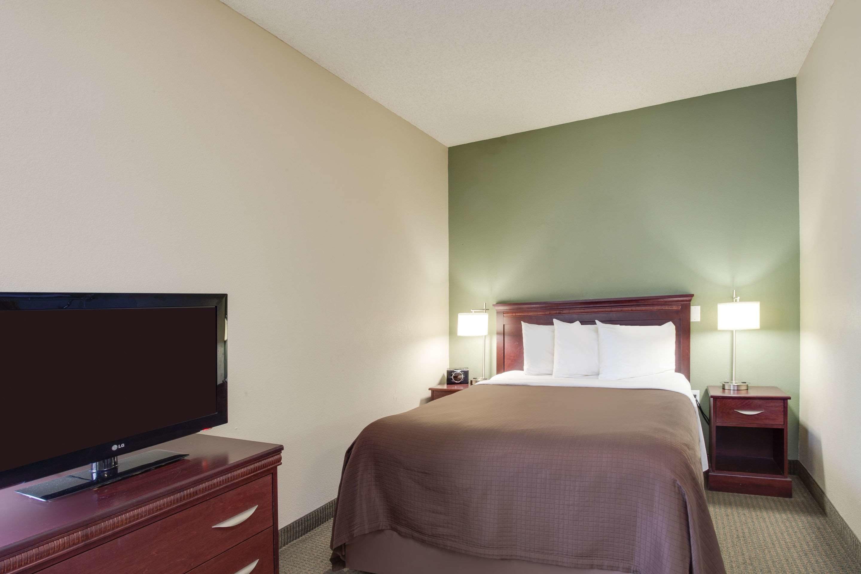 Une chambre d’hôtel avec un lit, un téléviseur posé sur une commode en bois, deux lampes de chevet et une table de chevet.
