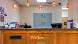 Una reception hotel con un cartello che riporta la scritta 'Welcome', un computer Dell e una segnaletica per l'ufficio.
