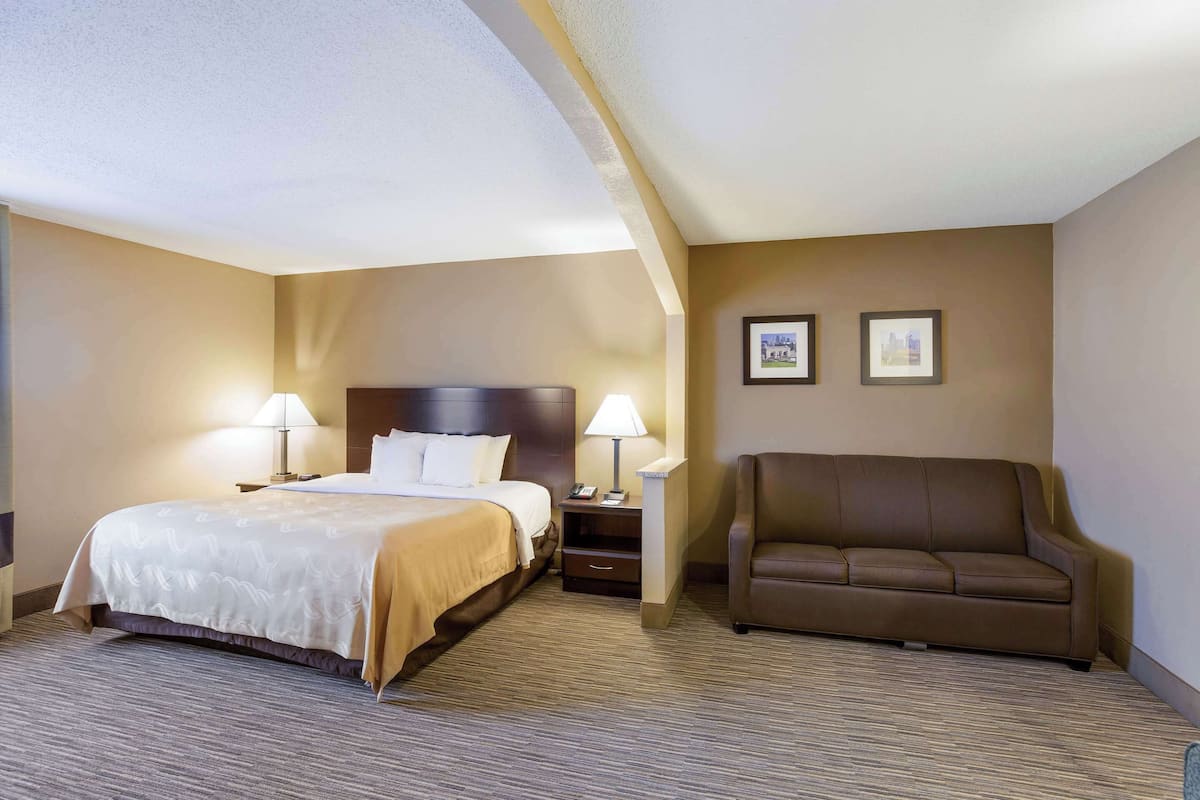A hotel room with a bed, two bedside lamps, a brown leather armchair, and two framed pictures on the wall.