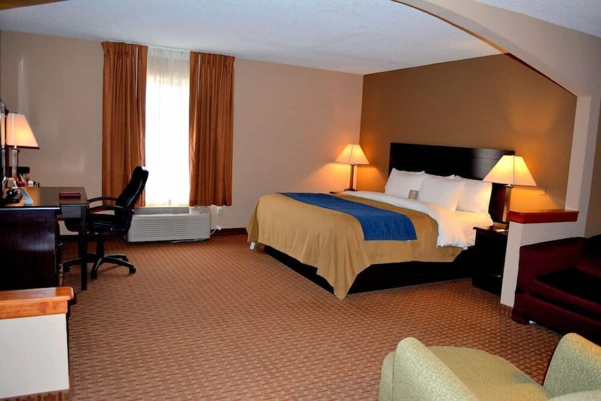 A hotel room with a bed, desk, chair, and a window with curtains.
