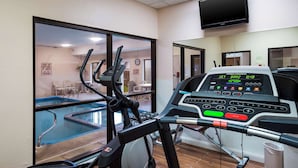 Una palestra con tapis roulant, piscina e televisore montato a parete.
