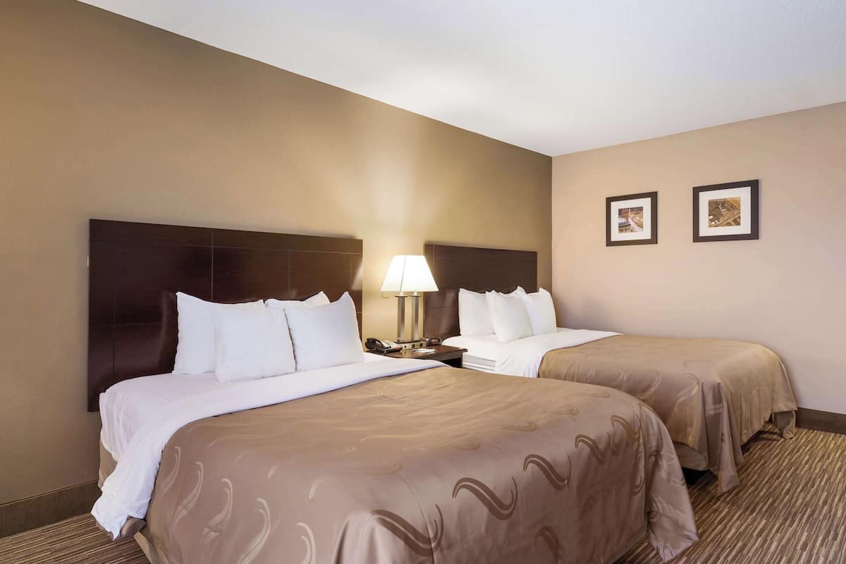 A hotel room with two beds, a nightstand with a lamp, and two framed pictures on the wall.