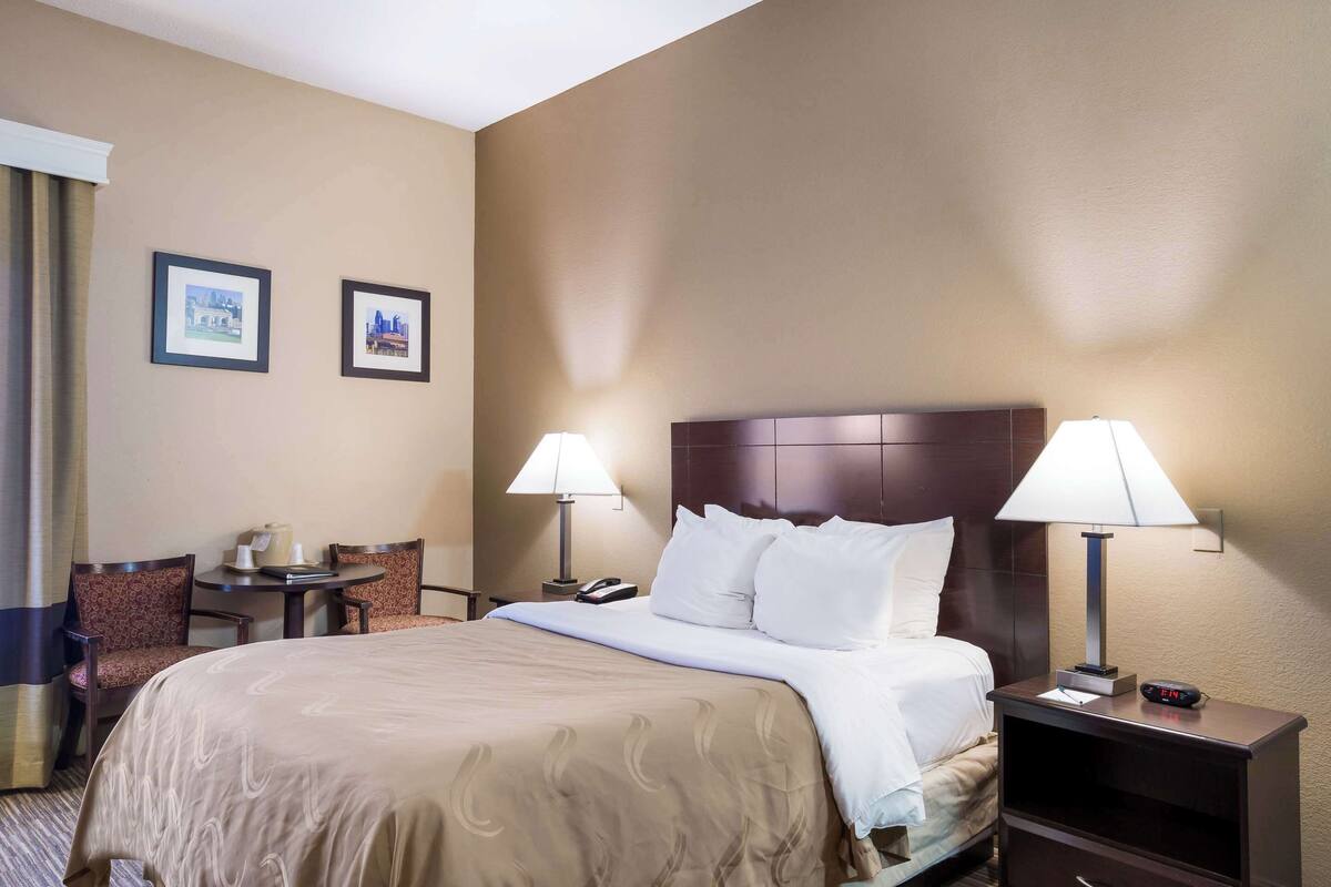 A hotel room with a large bed, two bedside tables with lamps, a chair, and two framed pictures on the wall.