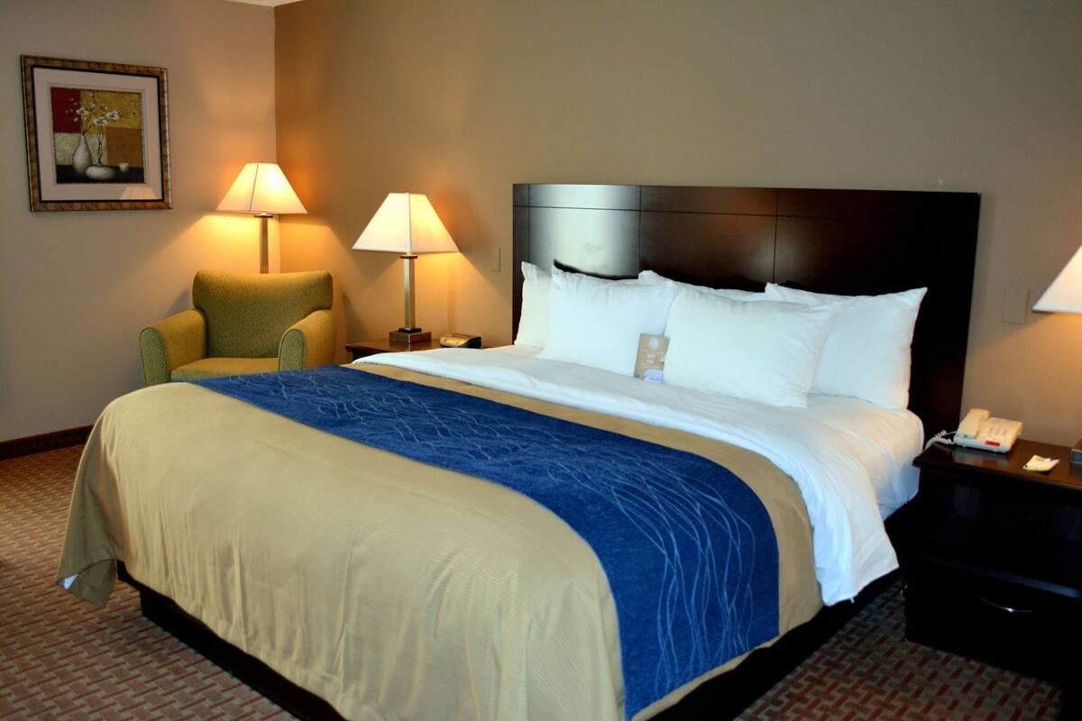 A hotel room with a large bed, two bedside lamps, a nightstand with a phone, and a chair.