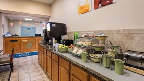 Un'area reception di un hotel con un cartello che dice 'Benvenuti', una macchina per il caffè e un buffet per la colazione con diversi cibi.