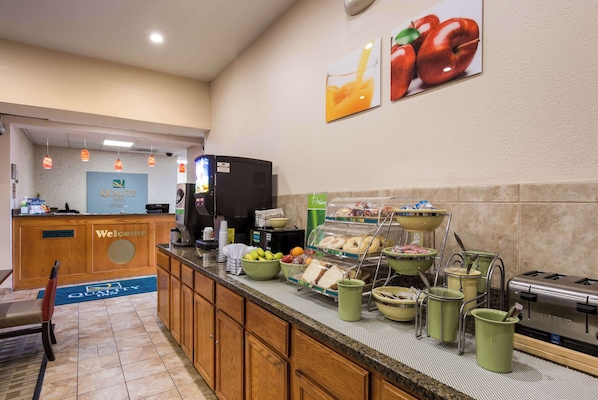 A hotel reception area with a 'Welcome' sign, a coffee machine, and a breakfast buffet with various food items. - Quality Inn I-70 Near Kansas Speedway (Kansas City)
