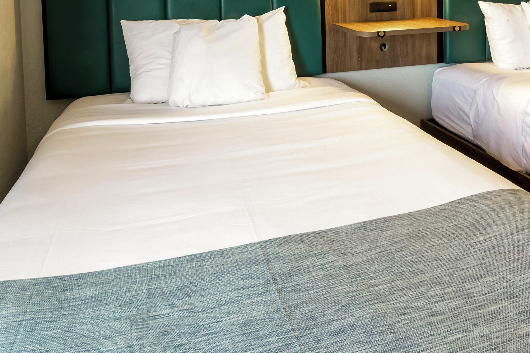 A hotel room with a large bed, a wooden shelf above it, and a green headboard.