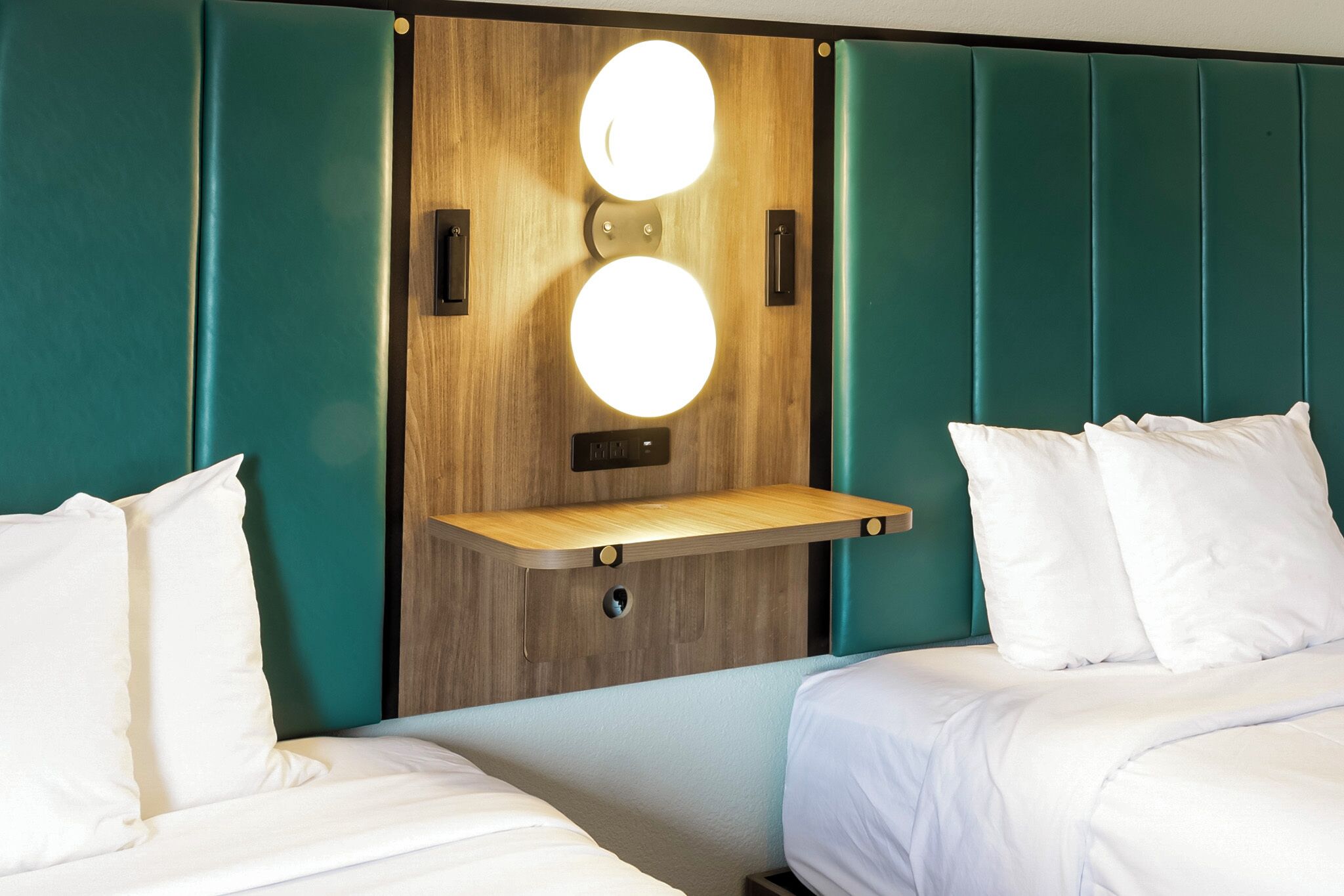 A hotel room with two beds, a wooden headboard with circular lights, and teal-colored walls.