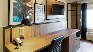 A modern office space with a wooden desk, a telephone, a flat-screen TV, and framed artwork on the wall. - Wingate by Wyndham Owensboro (Owensboro)