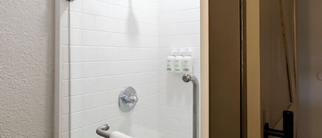 A shower area with white tiles, a handheld showerhead, a grab bar, and a towel rack.