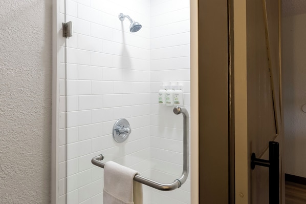 A shower area with white tiles, a handheld showerhead, a grab bar, and a towel rack.