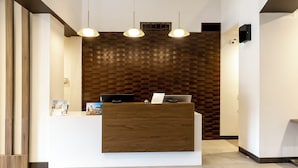 A reception desk with a wooden finish, two pendant lights, and a patterned wall behind it. - Wingate by Wyndham Owensboro (Owensboro)