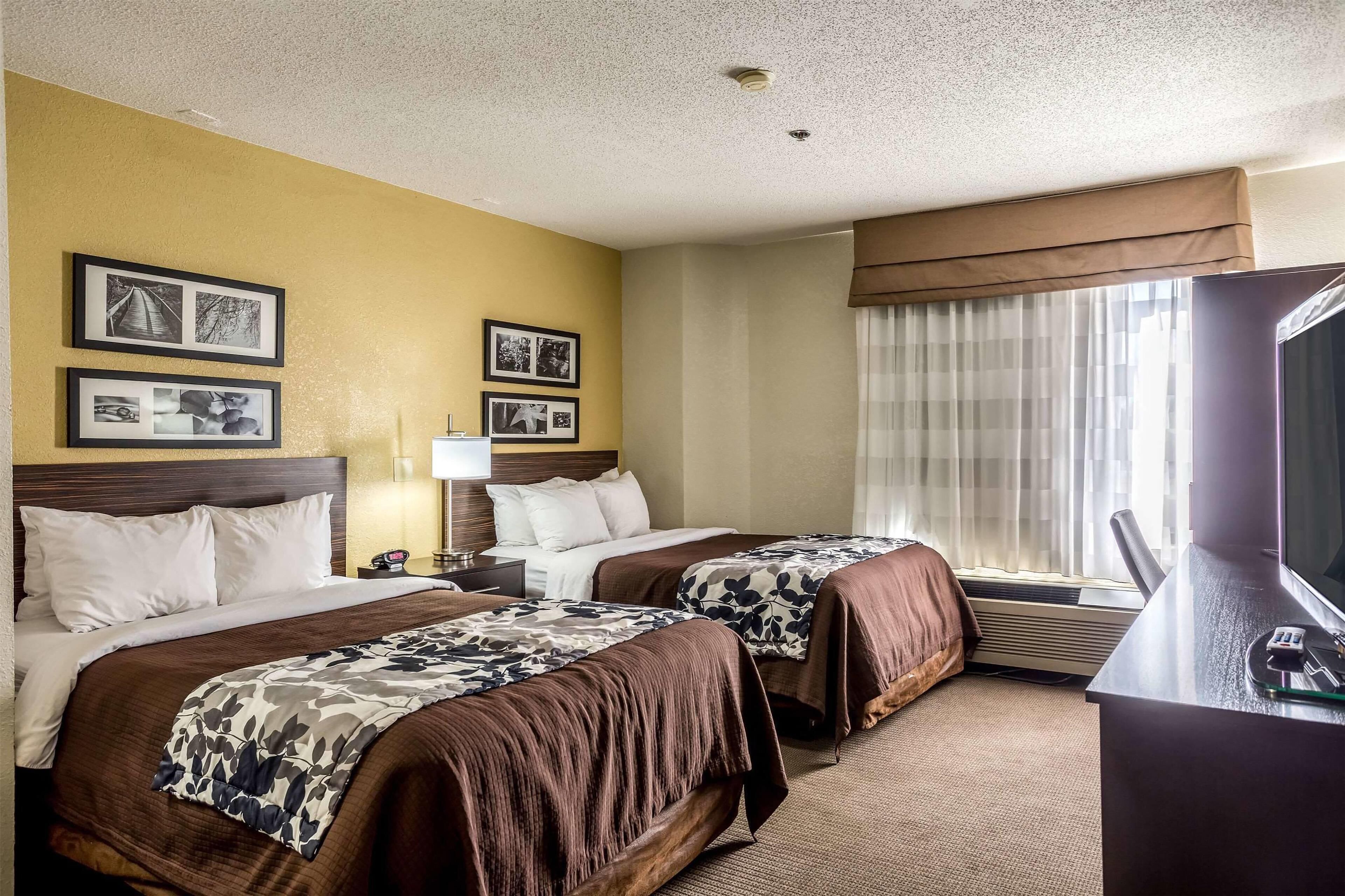 A hotel room with two beds, a desk with a TV, and framed pictures on the wall.