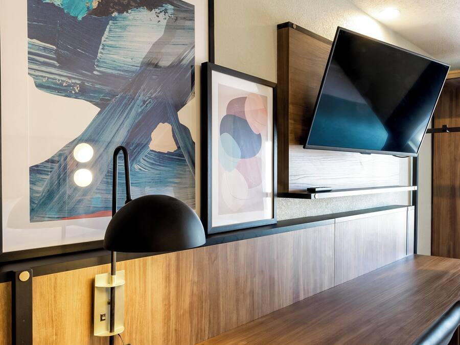 A modern room with a wooden desk, a mounted flat-screen TV, and two framed abstract artworks.