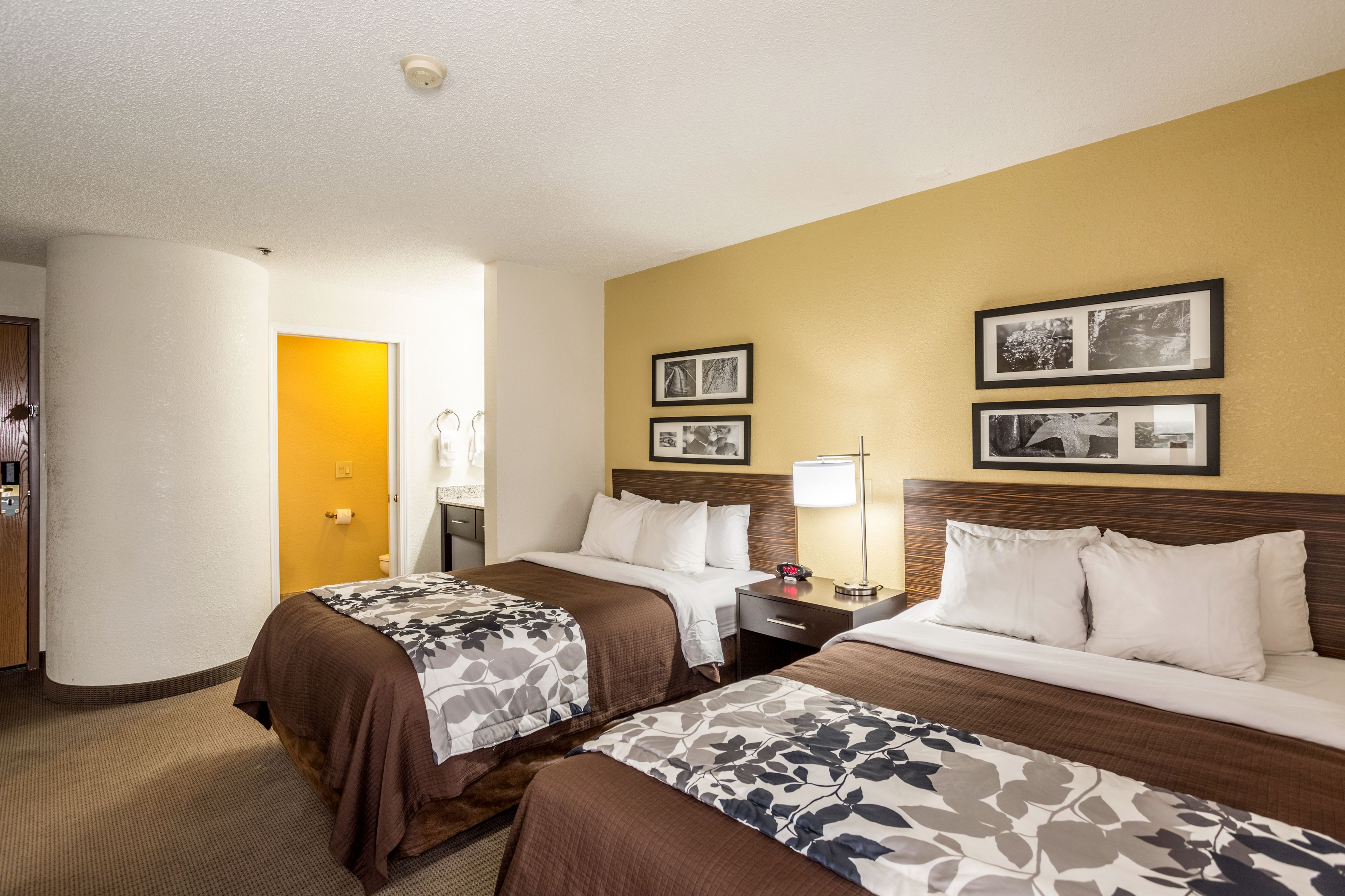 Een hotelkamer met twee bedden, een nachtkastje met een lamp en ingelijste foto's aan de muur.