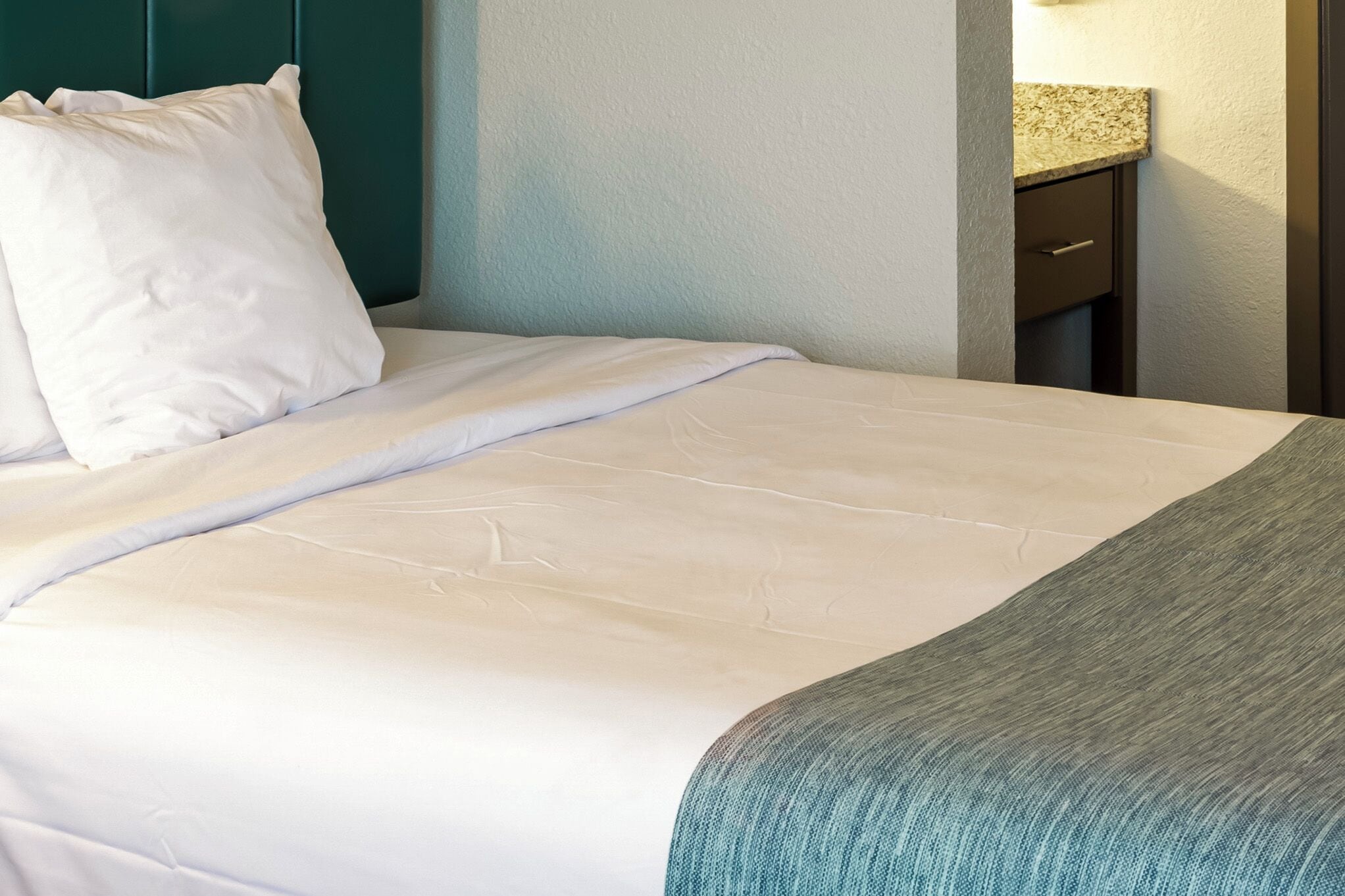 A neatly made bed with white linens and a teal throw blanket.