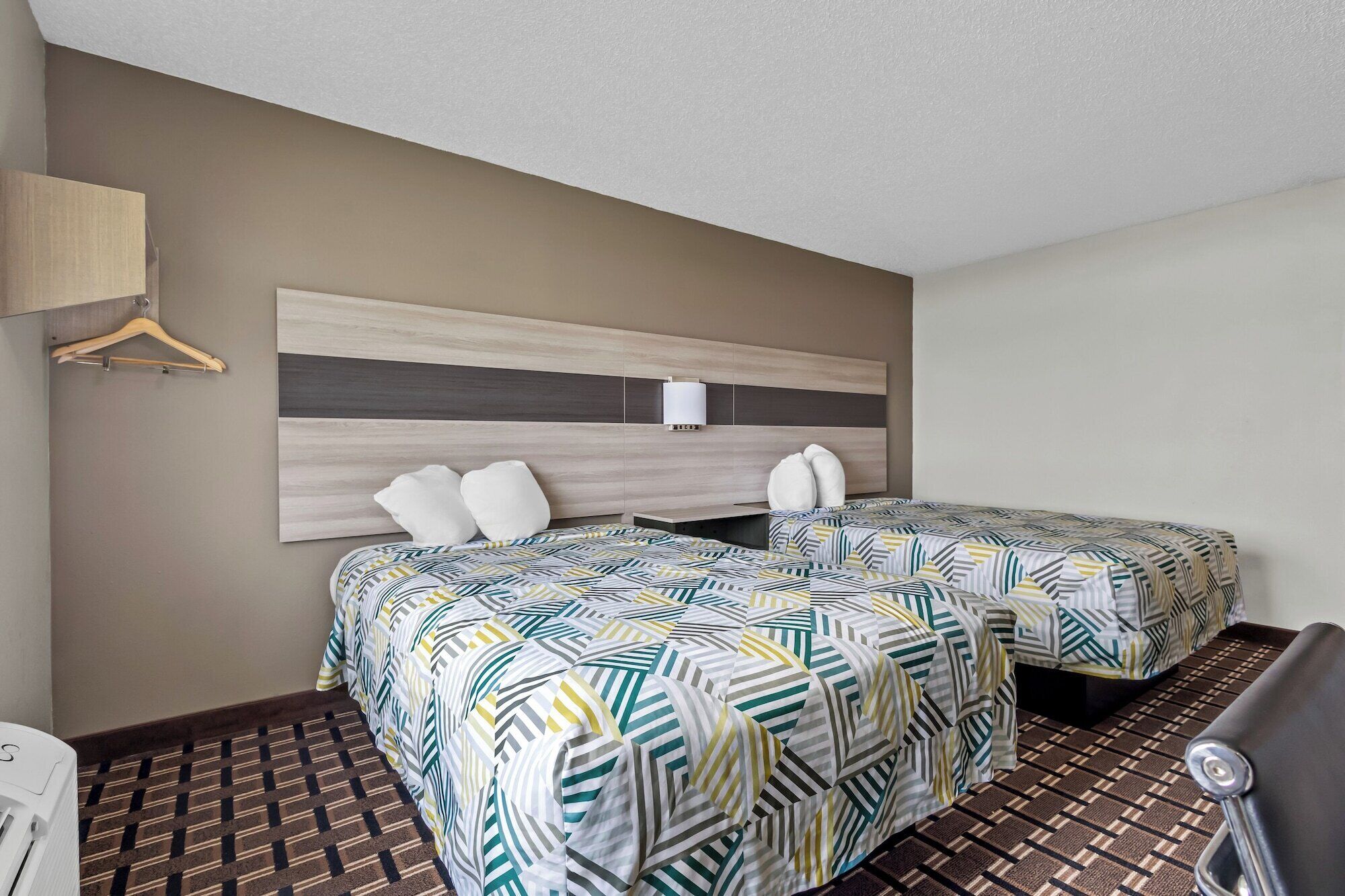 Une chambre d’hôtel avec deux lits, une tête de lit en bois, une lampe fixée au mur et un sol à motifs.