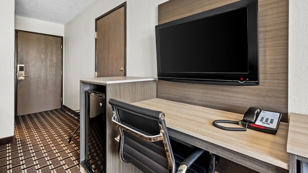 Ett hotellrum med ett skrivbord, en stol, en platt-TV och en telefon.