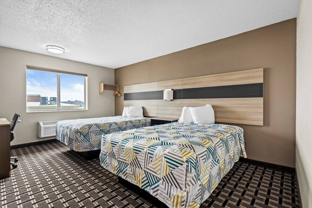 A hotel room with two beds, a large window, and a view of the outside.