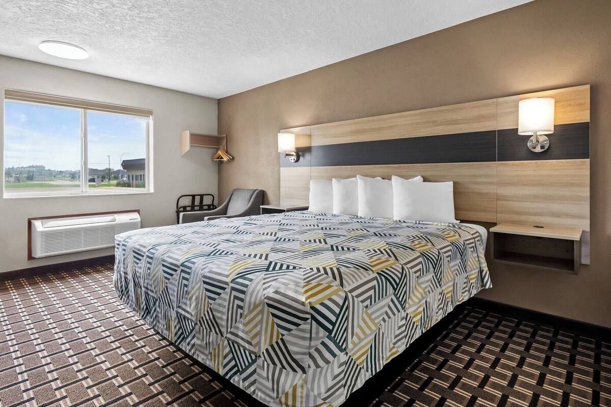 A hotel room with a large bed, a chair, a heater, a window with a view, and a wall-mounted light fixture.