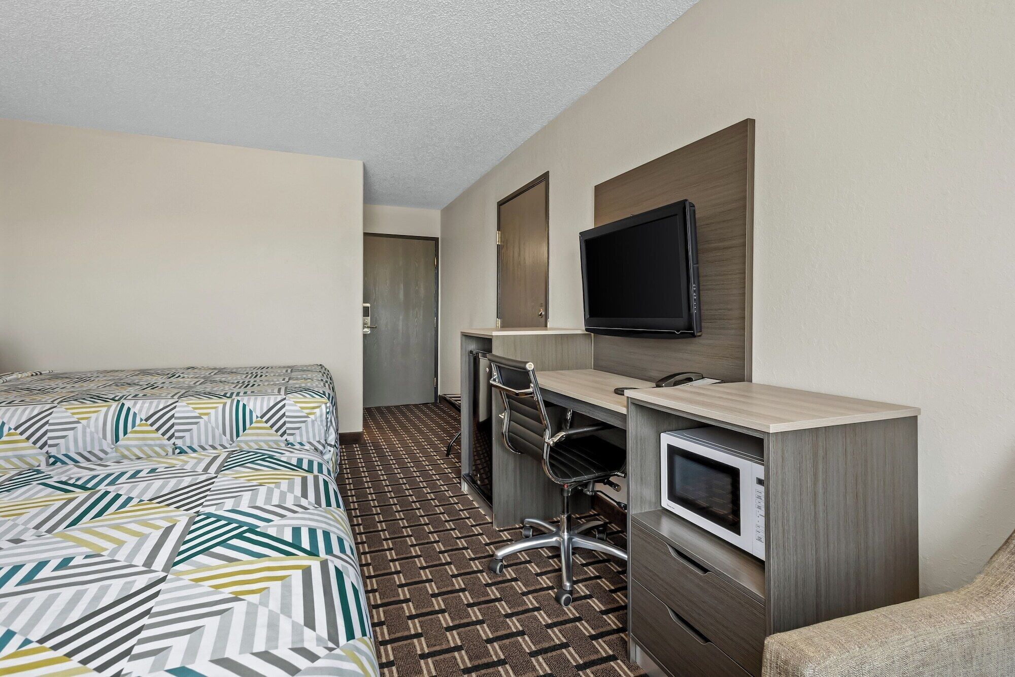 A hotel room with a bed, a desk with a chair, a television, and a microwave.