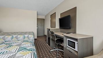 A hotel room with a bed, a desk with a chair, a television, and a microwave.
