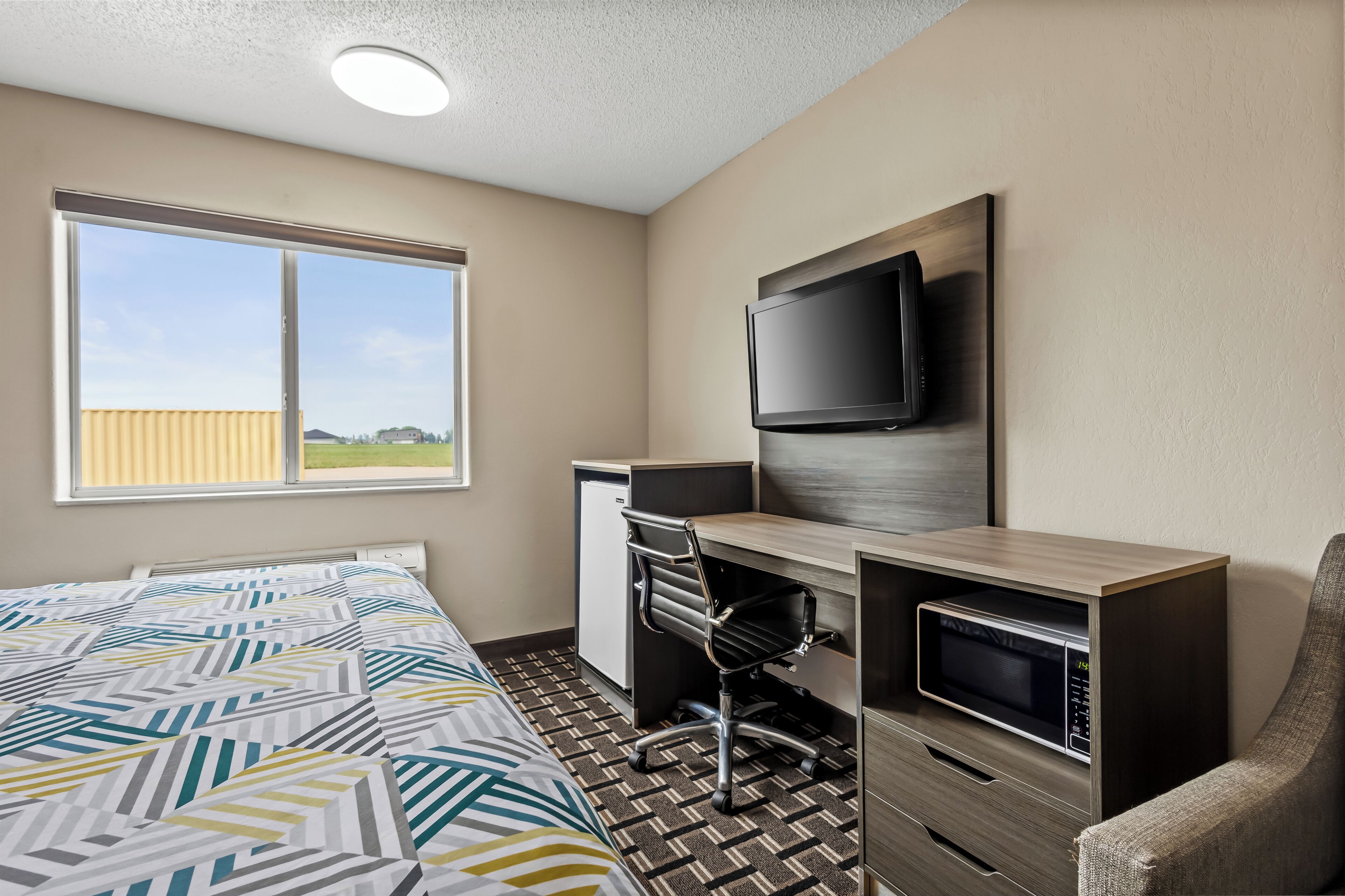 A hotel room with a bed, a desk with a computer, a TV, and a microwave.