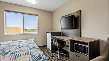 A hotel room with a bed, a desk with a computer, a TV, and a microwave.