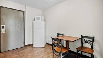 Una pequeña cocina americana equipada con microondas y refrigerador, una mesa de comedor de madera con dos sillas, y una puerta con picaporte.