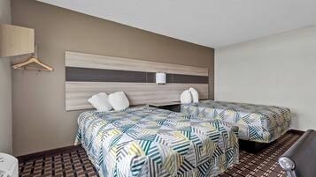 Habitación de hotel con dos camas, cabecero de madera, lámpara colgante y suelo estampado.