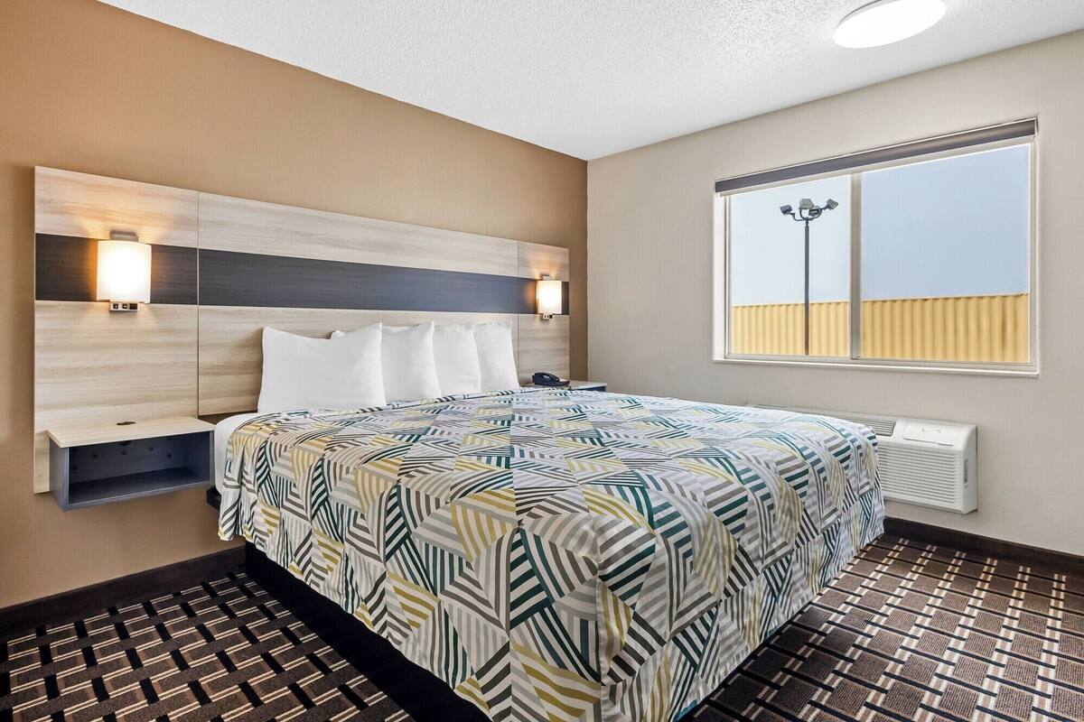 A hotel room with a bed, bedside table, lamp, and a window with a view.