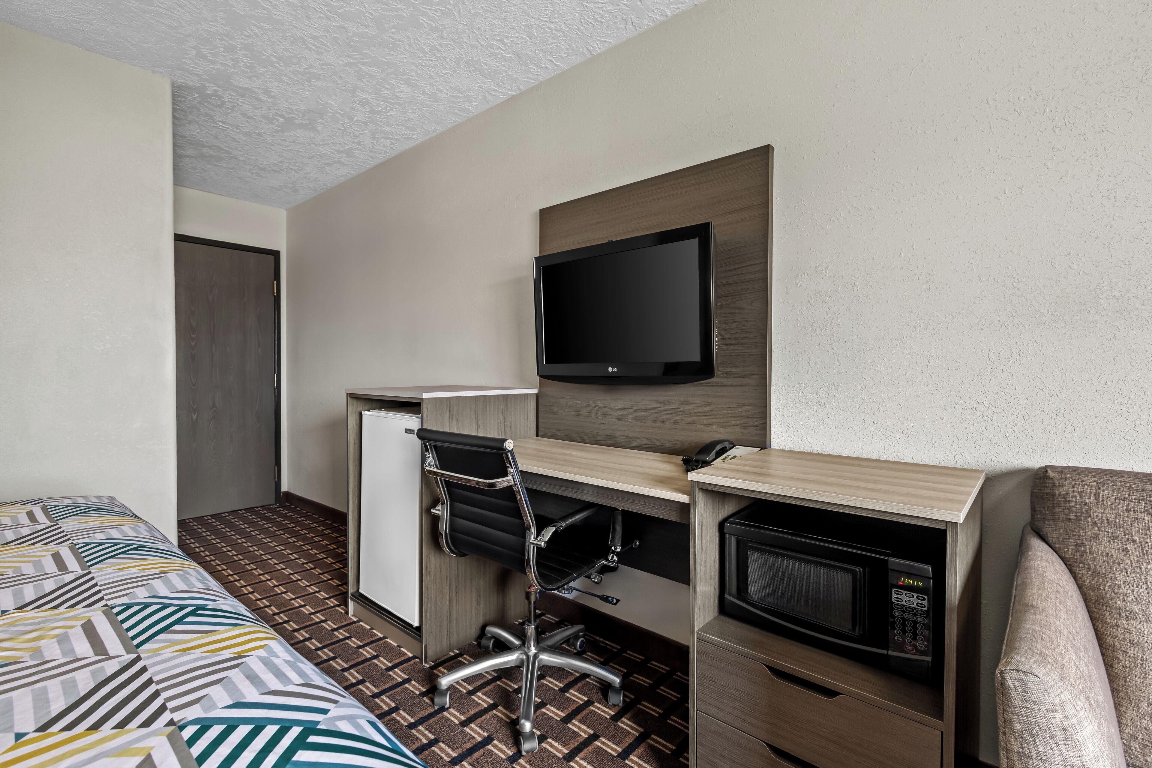 A hotel room with a bed, a desk with a chair, a television, a microwave, and a wardrobe.