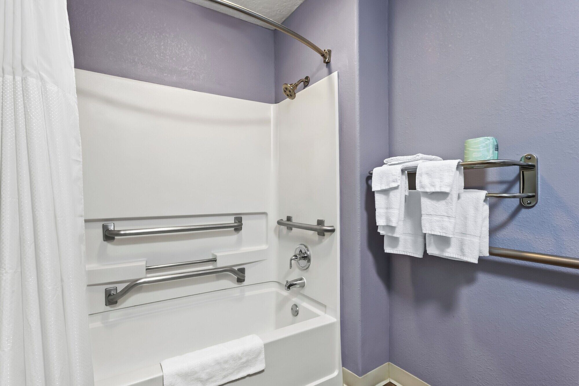 A bathroom with a bathtub, grab bars, a towel rack with towels, and a shower head.