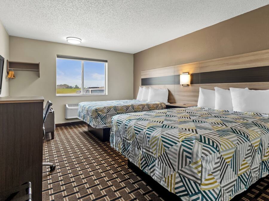 Habitación de hotel con dos camas, un escritorio, televisor y ventana con vistas, además de alfombra estampada.