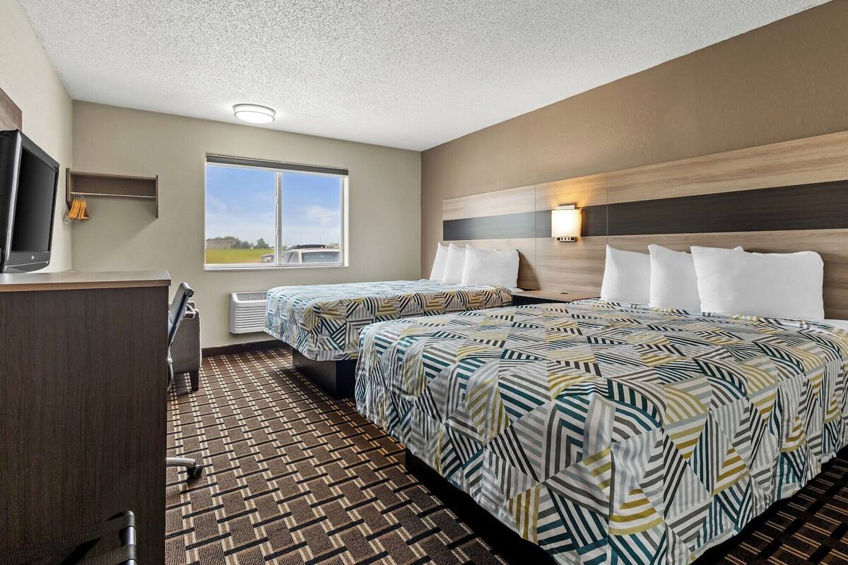 A hotel room with two beds, a desk, a television, and a window with a view of the outdoors.