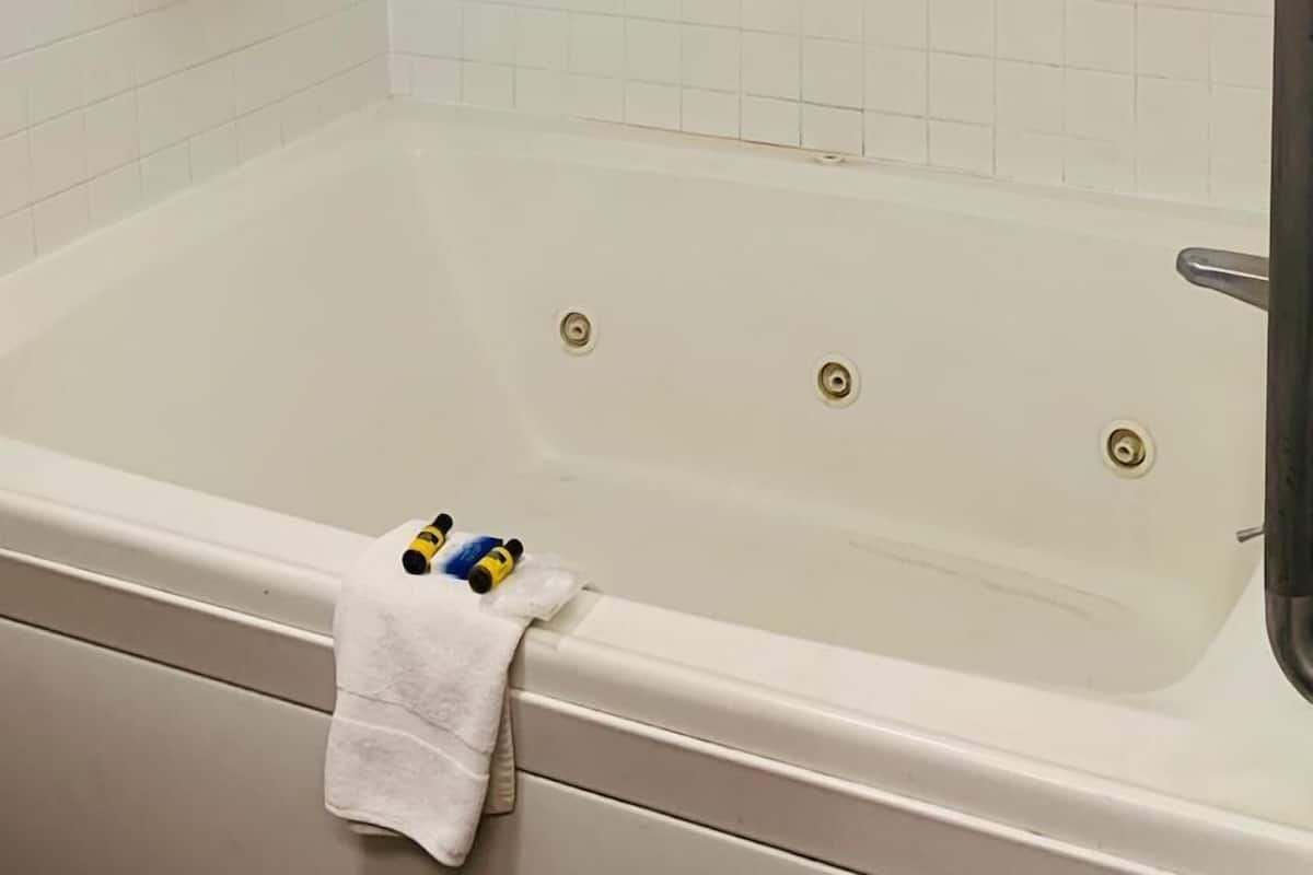 Un baño con pared de ducha en blanco, una bañera y una toalla colgada a un lado, además de un pasamanos metálico sobre la bañera.