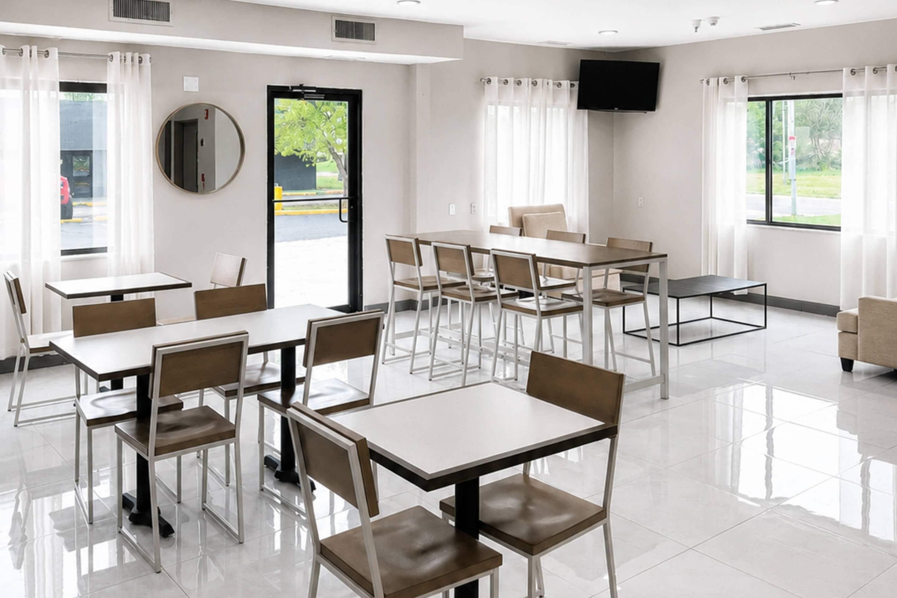A modern hotel room with a dining area, large windows, and a flat-screen TV.