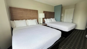 Una habitación de hotel con dos camas, una mesita de noche con lámpara y una puerta.
