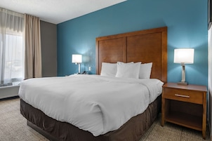 Habitación de hotel con una cama grande, cabecera de madera, dos lámparas de noche y una mesita de noche con cajón.