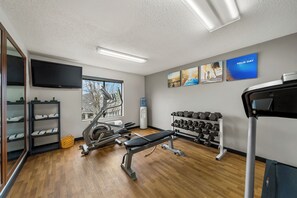 A gym with exercise equipment, a bench, a water dispenser, and artwork on the walls. - Comfort Inn Plainfield - Indianapolis Airport (Plainfield)