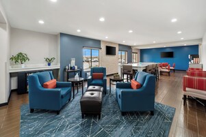 Un moderno vestíbulo de hotel con sofás azules, una máquina de café, un televisor y vistas al estacionamiento.