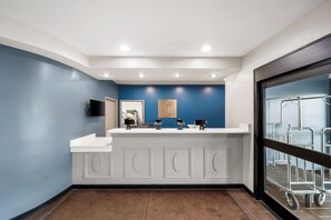 A reception area with a blue accent wall, a white reception desk, and a large window with metal chairs outside. - Comfort Inn Plainfield - Indianapolis Airport (Plainfield)