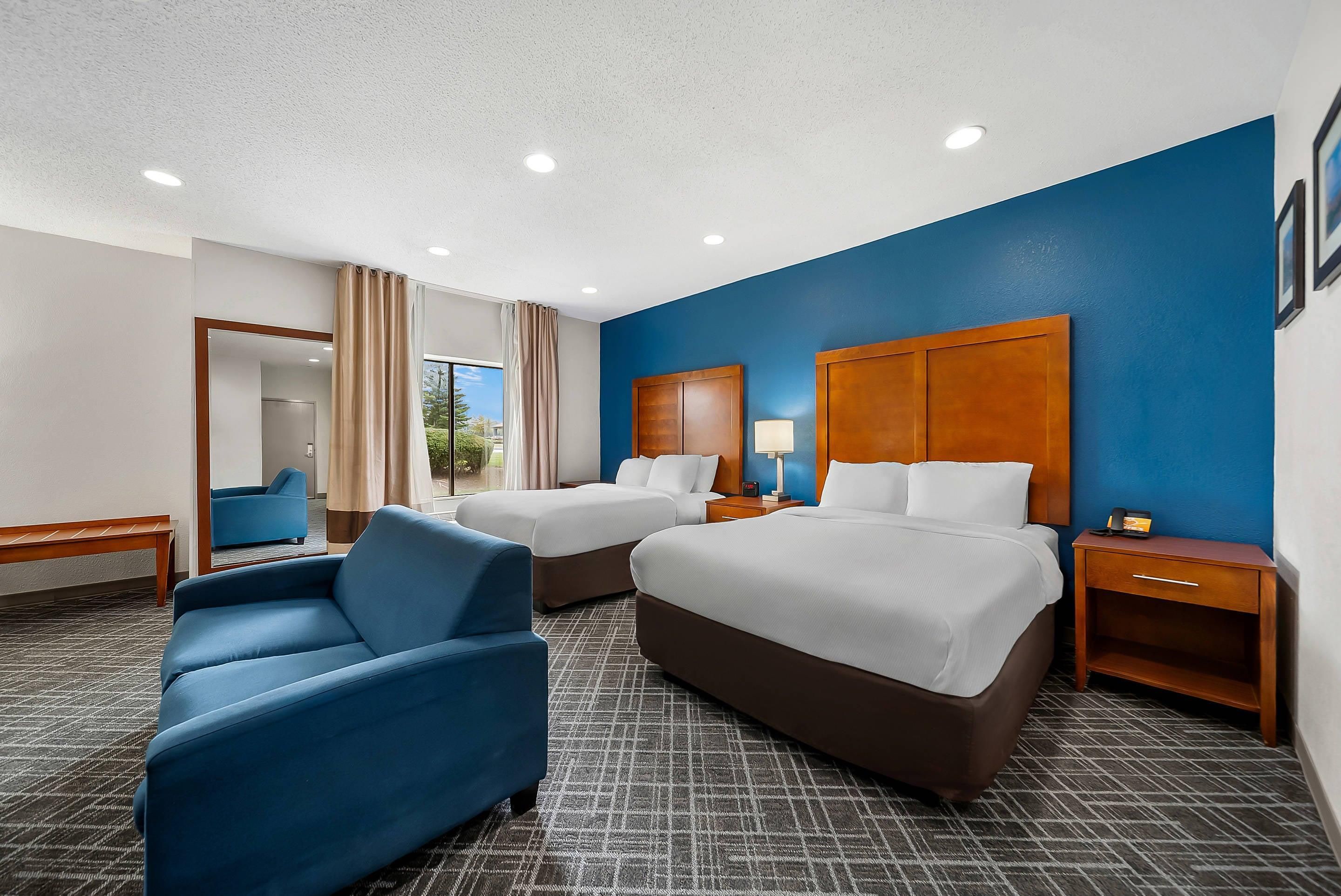 Ein Hotelzimmer mit zwei Betten, einem blauen Sessel, einem Nachttisch und einem großen Fenster.