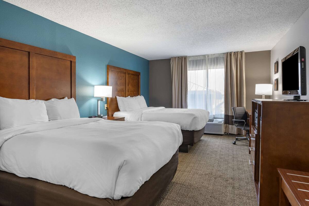 A hotel room with two beds, a desk, a TV, and a window with curtains.