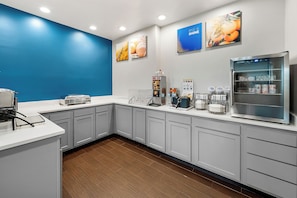 A modern kitchen with grey cabinets, a stainless steel refrigerator, and a blue accent wall. - Comfort Inn Plainfield - Indianapolis Airport (Plainfield)