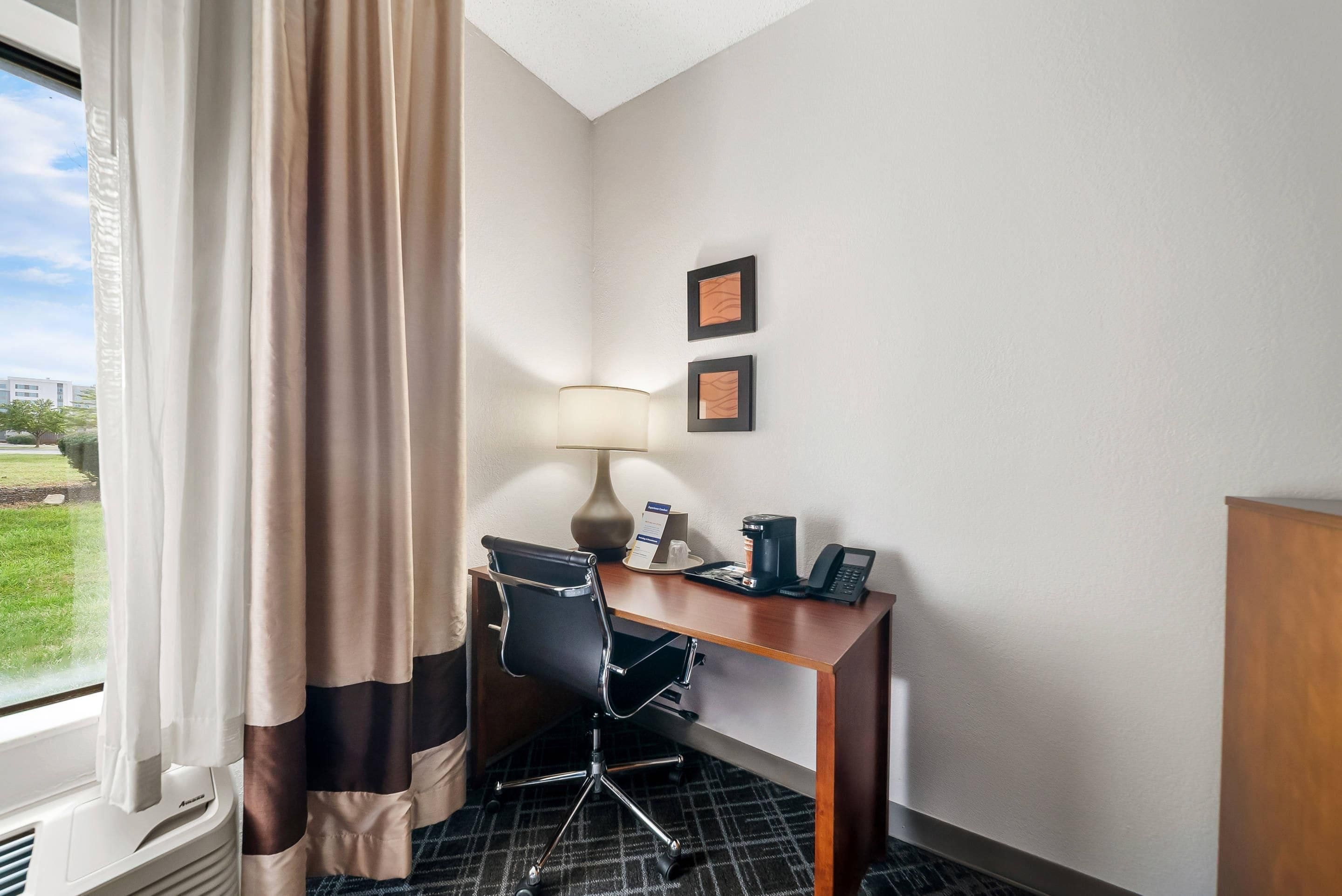 Une chambre d’hôtel équipée d’un bureau, d’une chaise, d’une lampe, d’une machine à café, d’un téléphone et de deux tableaux encadrés accrochés au mur.