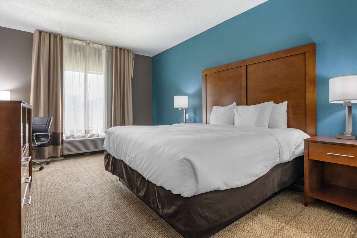 A hotel room with a large bed, a desk, a chair, and a window with curtains.