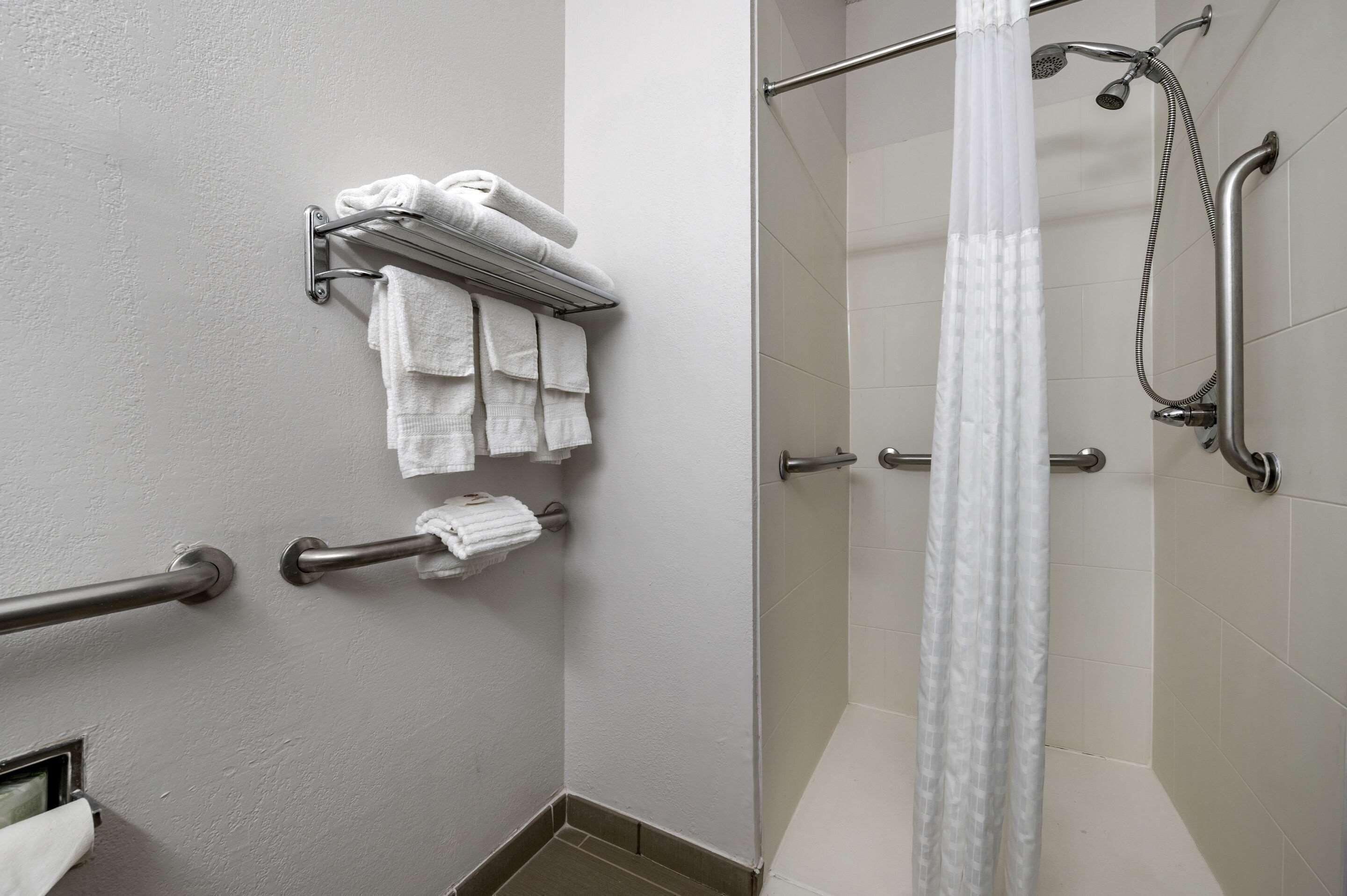 A bathroom with a shower, a towel rack with folded towels, and a handrail.